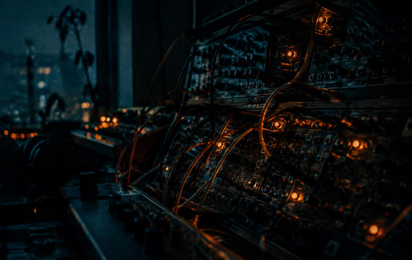 Analogue modular synthesizer with patch cables and amber lights in a dark studio